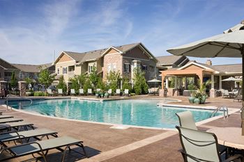 a swimming pool with chairs and umbrellas in front of a house at Sovereign at Overland Park, Overland Park Kansas